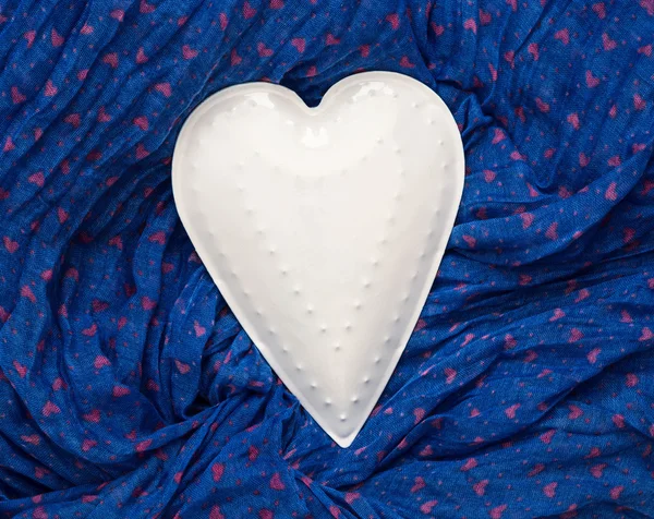 Bílý kov srdce leží na modrou tkaninou — Stock fotografie