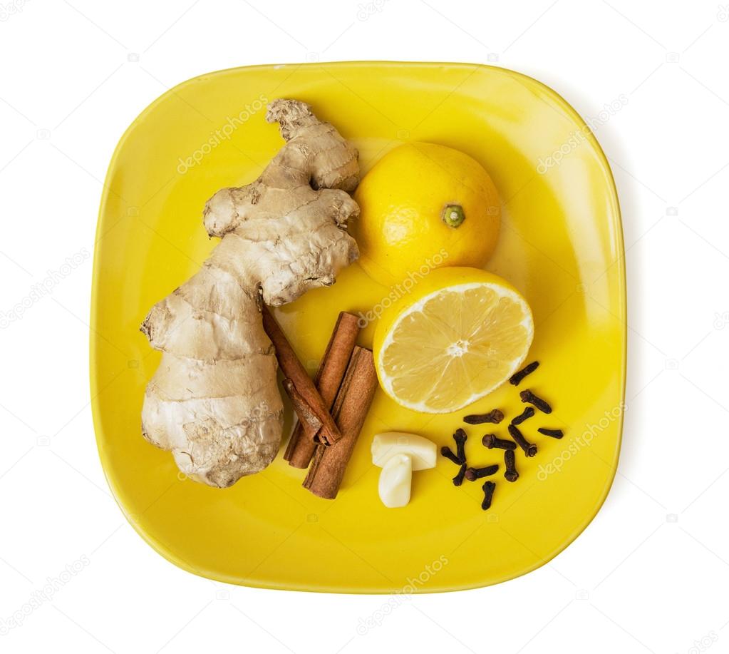 Ginger, cinnamon, lemon, garlic and cloves on the yellow plate