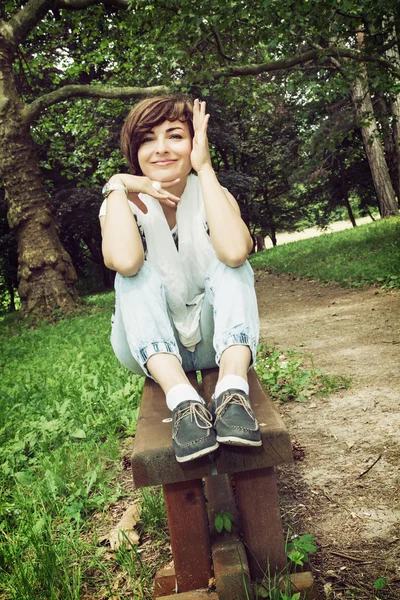 Young joyful brunette sitting on the park bench — Stock Photo, Image