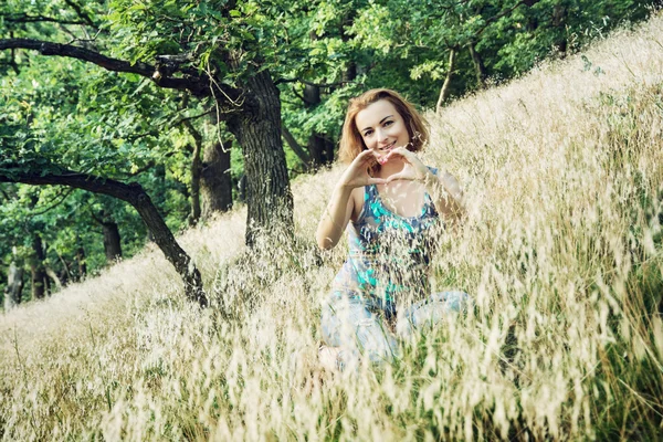 Attractive woman makes heart shape with her hands in the forest — Stock Photo, Image