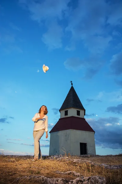 Young woman throws up her hat by sunset near the church — Stock Photo, Image