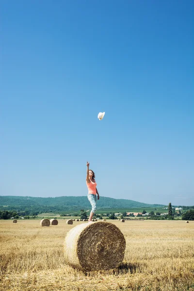 Young woman stands on the haystack and throws her hat high into — Stock Photo, Image