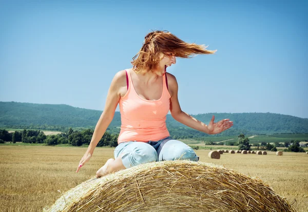 Young crazy woman sits on the stack of straw and throws with her — Stockfoto