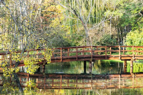 Wooden bridge over mirrored lake in the beautiful autumn park — Stockfoto