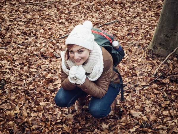 Jeune femme en casquette blanche squats dans les feuilles brunes à la fores — Photo