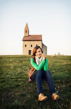 Young woman is sitting in front of the church clipart