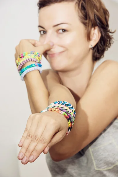 Jonge vrouw met kleurrijke rubber armbanden op haar handen maakt een — Stockfoto