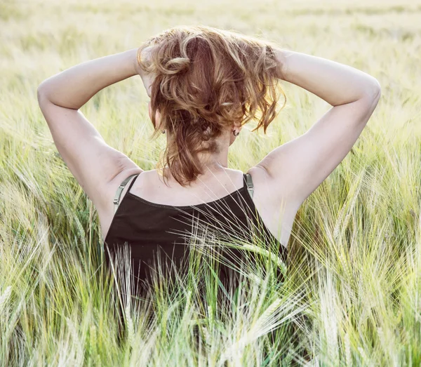 Mujer joven sostiene su cabello al atardecer en el campo, vista trasera — Foto de Stock