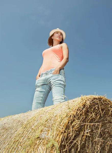 Young woman is standing on the stack of straw and looking left — Stock Photo, Image