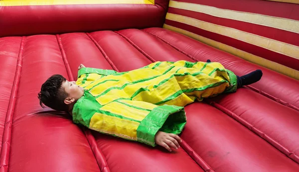 O menino em vestido de plástico colorido está deitado no castelo bouncy — Fotografia de Stock