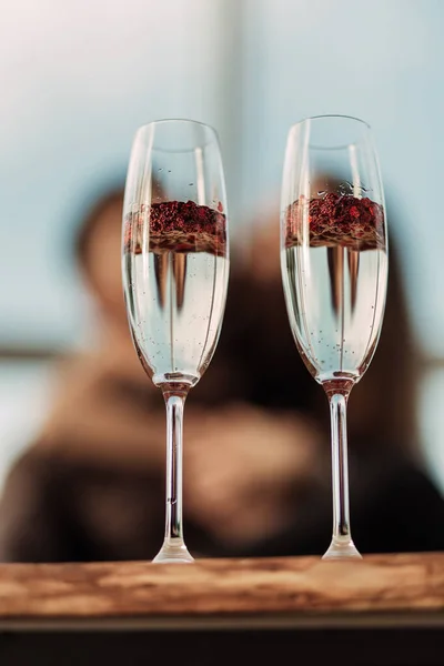 Feliz día de San Valentín concepto de celebración. Primer plano de 2 dos copas con champán espumoso y confeti rojo en forma de corazón. Poción de amor en vidrio. Pareja amorosa borrosa en el fondo —  Fotos de Stock