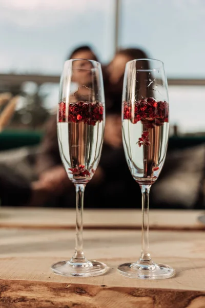 Feliz día de San Valentín concepto de celebración. Primer plano de 2 dos copas con champán espumoso y confeti rojo en forma de corazón. Poción de amor en vidrio. Pareja amorosa borrosa en el fondo —  Fotos de Stock