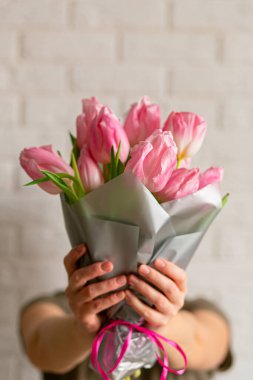 Beyaz tuğla duvarın yanında pembe laleleri olan güzel bir kadın. Metin için yeri olan yakın plan. Bahar tebrik kartı. Uluslararası Kadınlar Günü kavramı, Anneler Günü, Paskalya. Boşluğu kopyala