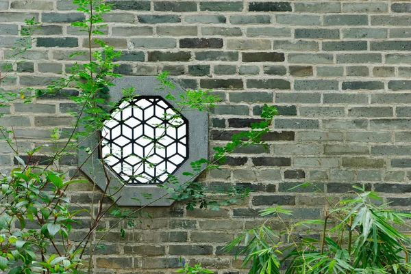 Round Chinese window on wall in garden with bamboo