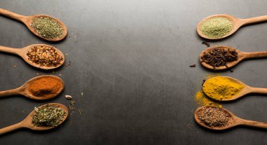 Tahta kaşıklardaki çeşitli baharatlar, kopya alanı olan taş masadaki.