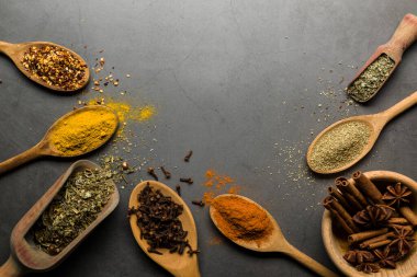 Tahta kaşıklarda çeşitli baharatlar, kopyalama alanı olan gri masada.
