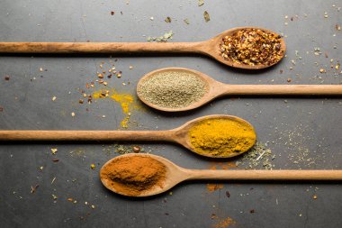 Tahta kaşıklarda, taş masada çeşitli baharatlar.