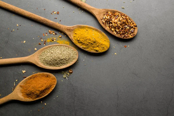 Tahta kaşıklardaki çeşitli baharatlar, kopya alanı olan taş masadaki.
