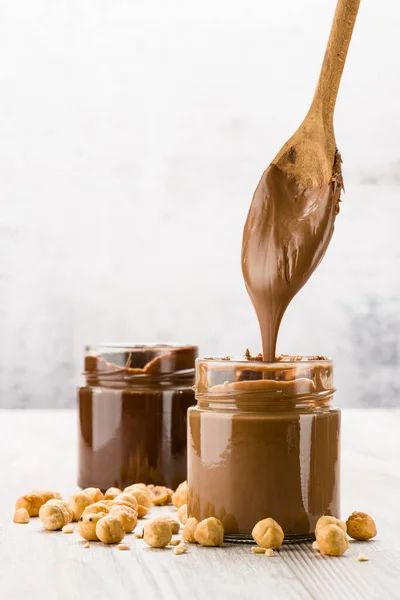 Crema Cioccolato Barattolo Vetro Con Nocciole Cucchiaio Sgocciolante Tavolo Legno — Foto Stock