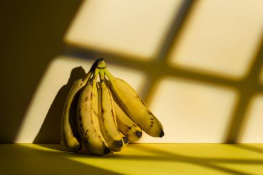 Sarı zemin üzerinde bir sürü olgun muz ve pencere ışığı efekti.