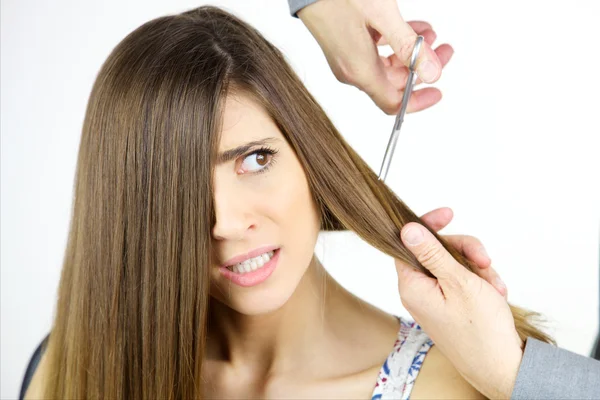 Mujer joven asustada de cortarse el pelo largo con tijeras aisladas — Foto de Stock