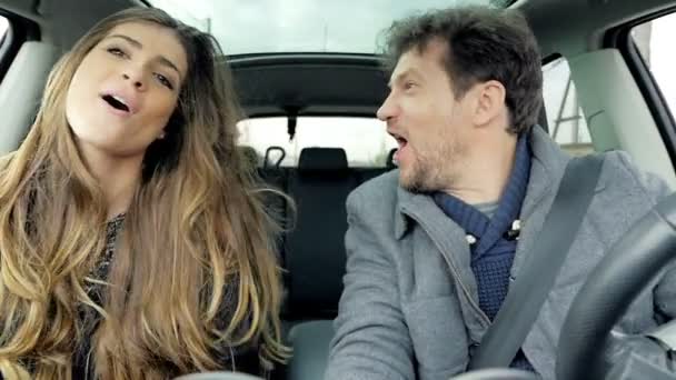 Счастливая пара поет и танцует во время вождения автомобиля глядя камеры замедленной съемки — стоковое видео