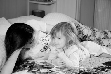 Siyah beyaz portre bir anne ile kızı yatakta eğleniyor