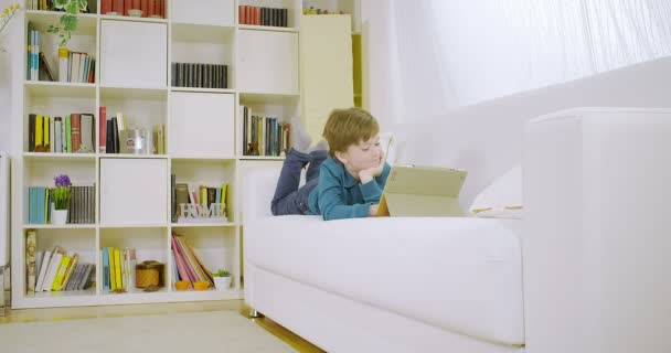 Niño disfrutando del juego en la tableta en casa en el sofá 4K — Vídeo de stock