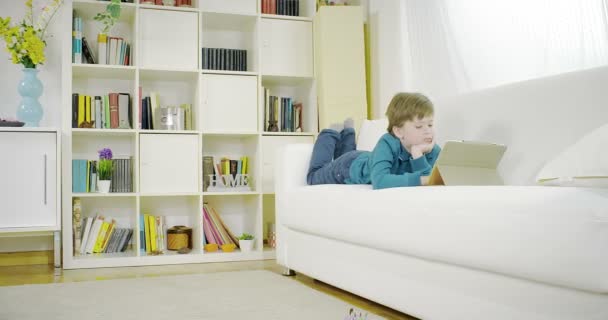 Chlapec si hru na tabletu doma na gauči 4k — Stock video