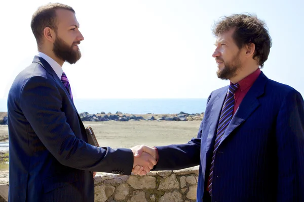 Two handsome business men shaking hand in front of the ocean — Stock Photo, Image