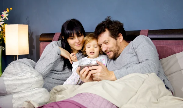 Счастливая семья в постели играет с телефоном — стоковое фото