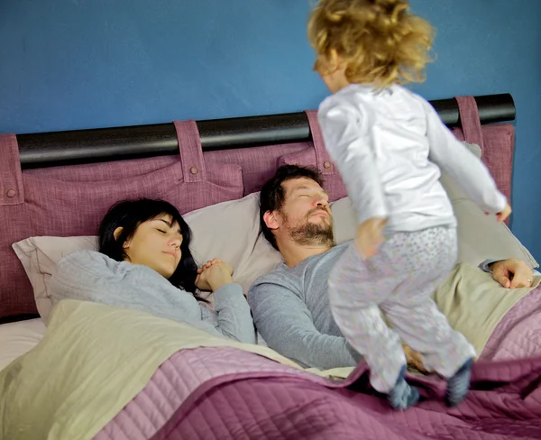 Маленькая девочка прыгает на кровати, пока родители спят — стоковое фото