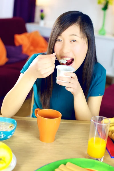 Happy chinese woman eating white yogurt — Stock Photo, Image