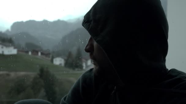 Triste hombre pensativo en la ventana en un día frío y lluvioso — Vídeos de Stock