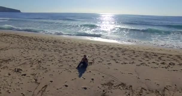 Tiro aéreo com drone de homem pensando sentado na praia em frente ao oceano — Vídeo de Stock