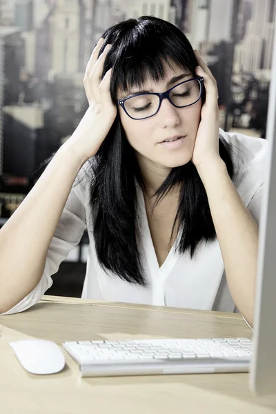 Mulher jovem sobrecarregada na frente do computador com dor de cabeça — Fotografia de Stock