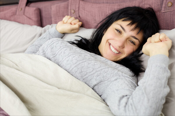 Happy smiling brunette lady waking up in bed