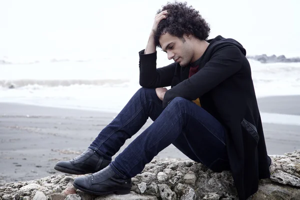 Önünde okyanus dalgaları ile kışın oturan üzgün yalnız adam — Stok fotoğraf