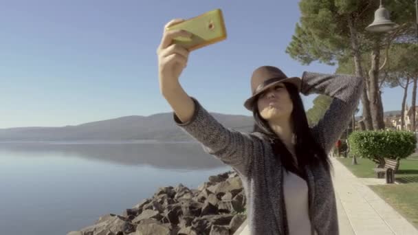 Câmera se movendo em torno bonito jovem com chapéu tomando selfie com telefone celular — Vídeo de Stock