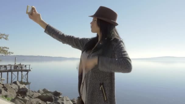 Słodkie młoda kobieta przy selfie przed jeziorem szczęśliwy kapelusz — Wideo stockowe