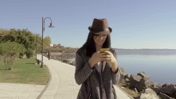 Mujer feliz caminando y hablando por teléfono frente al lago 4K — Vídeo de stock