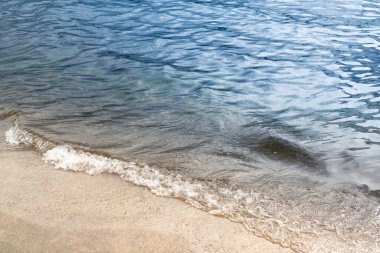 Kumsaldaki mavi denizde el salla.