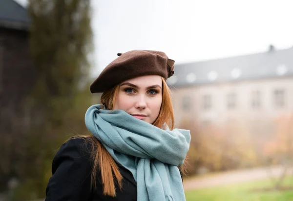 年轻女人带着棕色贝雷帽和蓝色围巾她在外面 看着摄像机 免版税图库图片