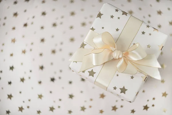 Cadeaudoosje met beige strikje op een lichte achtergrond met sterren. Vlakke lay met zachte focus. — Stockfoto