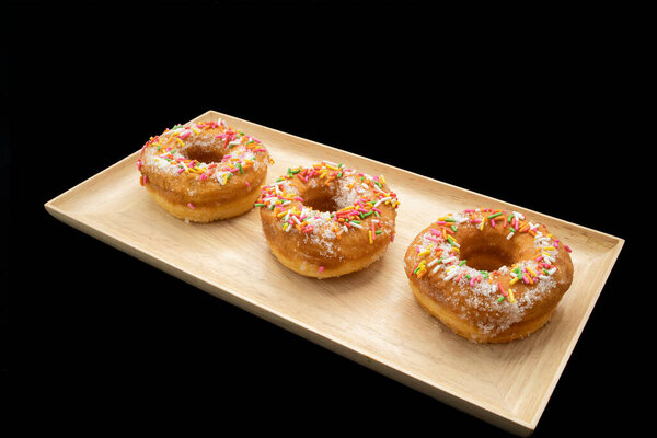 Traditional sugar donuts with multi color sprinkles on a wooden plate. 