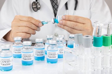 Laboratuvar önlüklü bir doktor ya da bilim adamı elinde sıvı aşı şişesi olan bir şırınga tutuyor. Covid-19 aşı kavramı