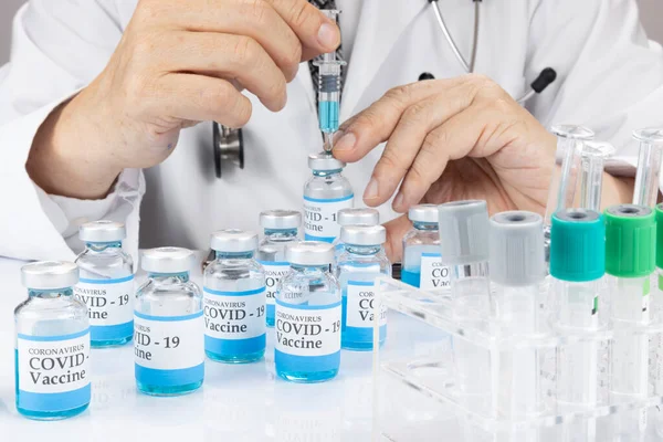 A doctor or a scientist in a laboratory coat holding a syringe with liquid vaccine vial.  Covid-19 vaccination concept.