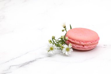 Beyaz mermer bir arka planda küçük beyaz çiçekli pembe bir badem kurabiyesi ya da Fransız kurabiyesinin kapağını kapatın..