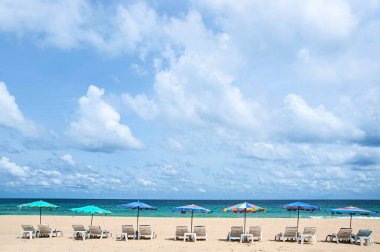 Mavi gökyüzünün altında turkuaz mavi deniz beyaz bulutlar ve renkli plaj şemsiyeleriyle Phuket 'teki Kata plajında. Tayland