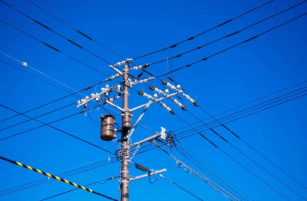 Yüksek voltaj kabloları elektrik direğinde çok yönlü transformatörle parlak mavi gökyüzüne karşı.